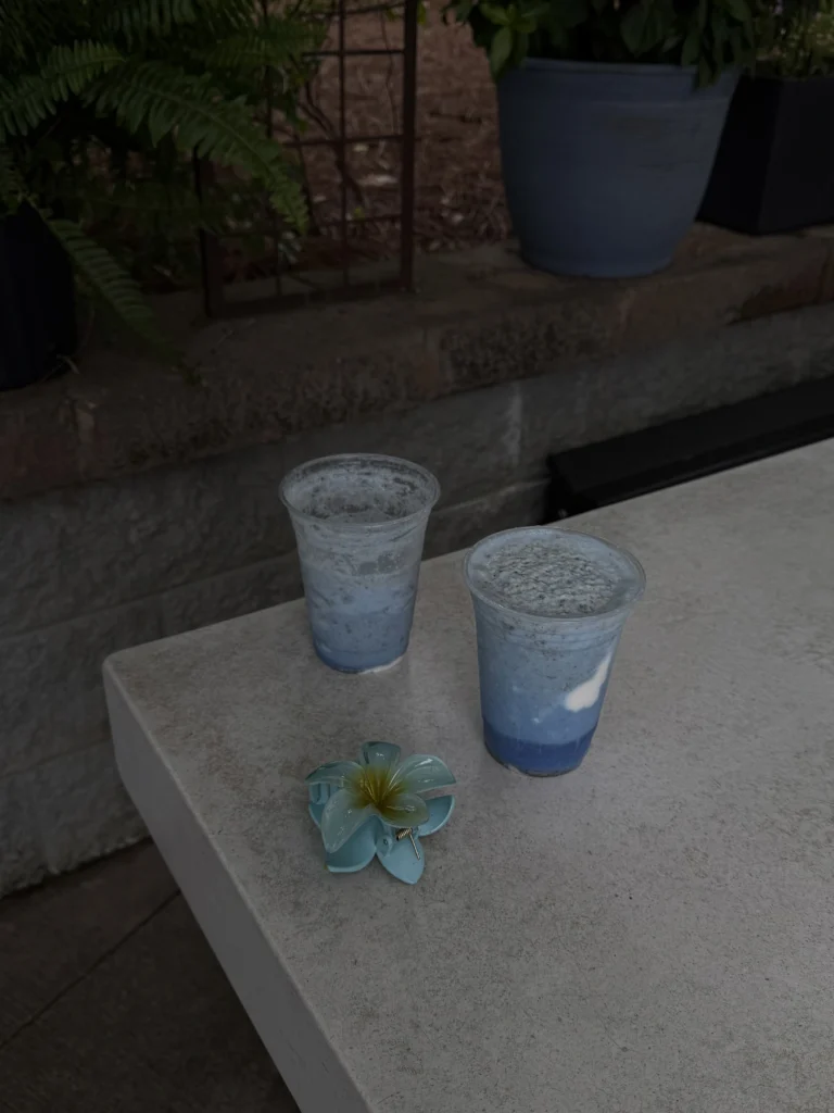 Two clear cups of blue layered smoothies with coconut swirl and flower.