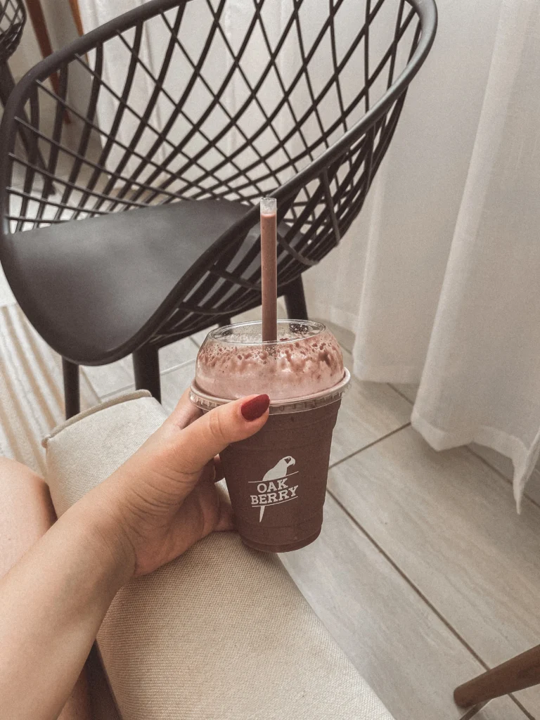 Hand holding chocolate açaí protein shake in a takeout cup.