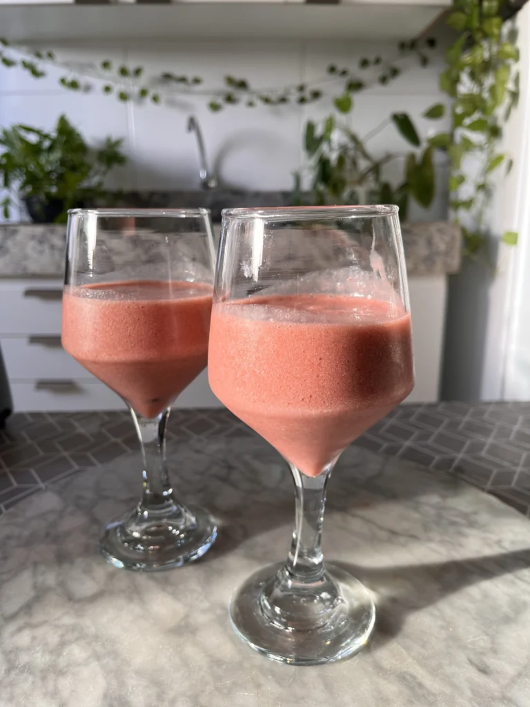 Two pink strawberry yogurt smoothies in stemmed glasses on counter.