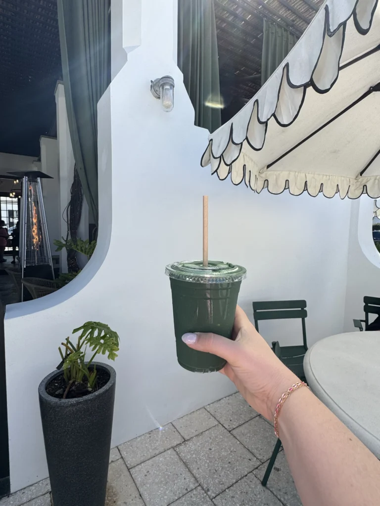 Hand holding deep green detox smoothie outside cafe
