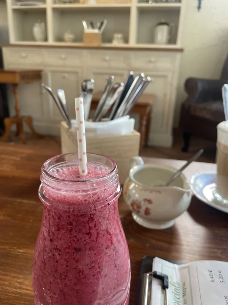 Magenta berry smoothie in café jar with dotted straw on wooden table.