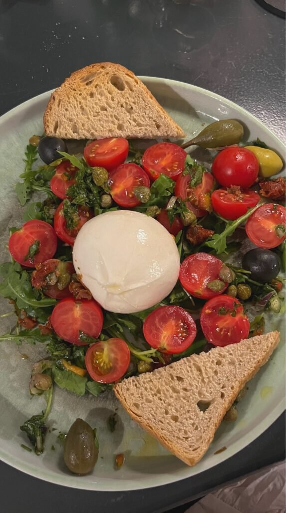 Burrata on arugula with cherry tomatoes, capers, olives, and rustic toast.