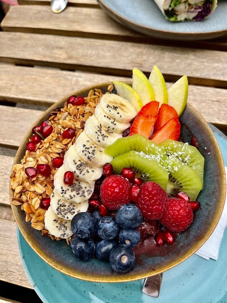 Colorful breakfast bowl with banana, kiwi, berries, pomegranate, granola, and chia seeds.