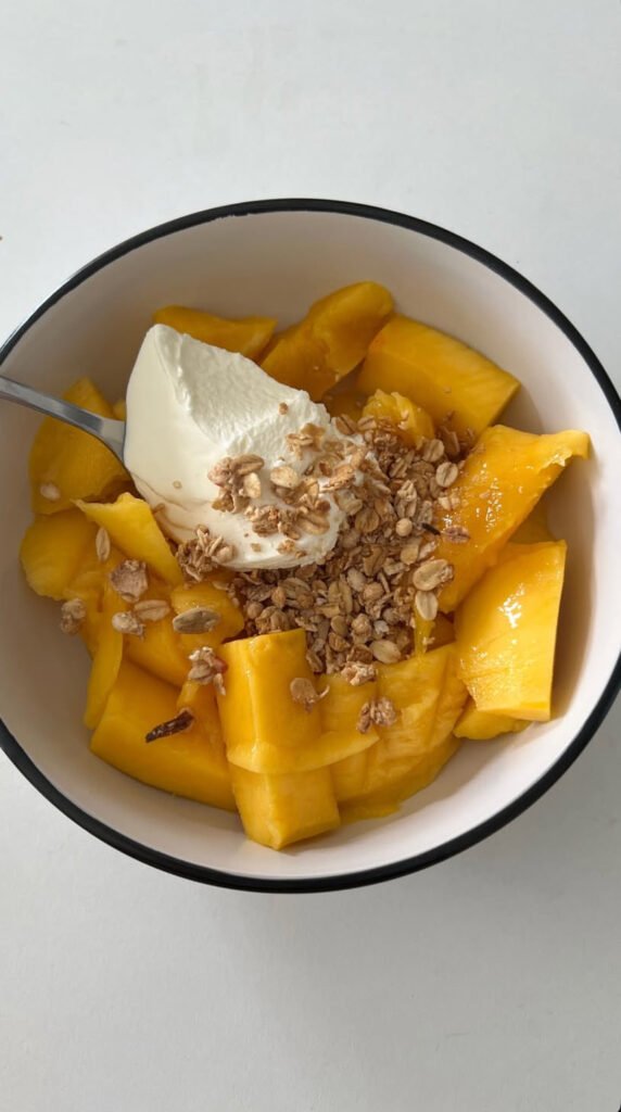 Bowl of ripe mango with creamy yogurt and crunchy granola.