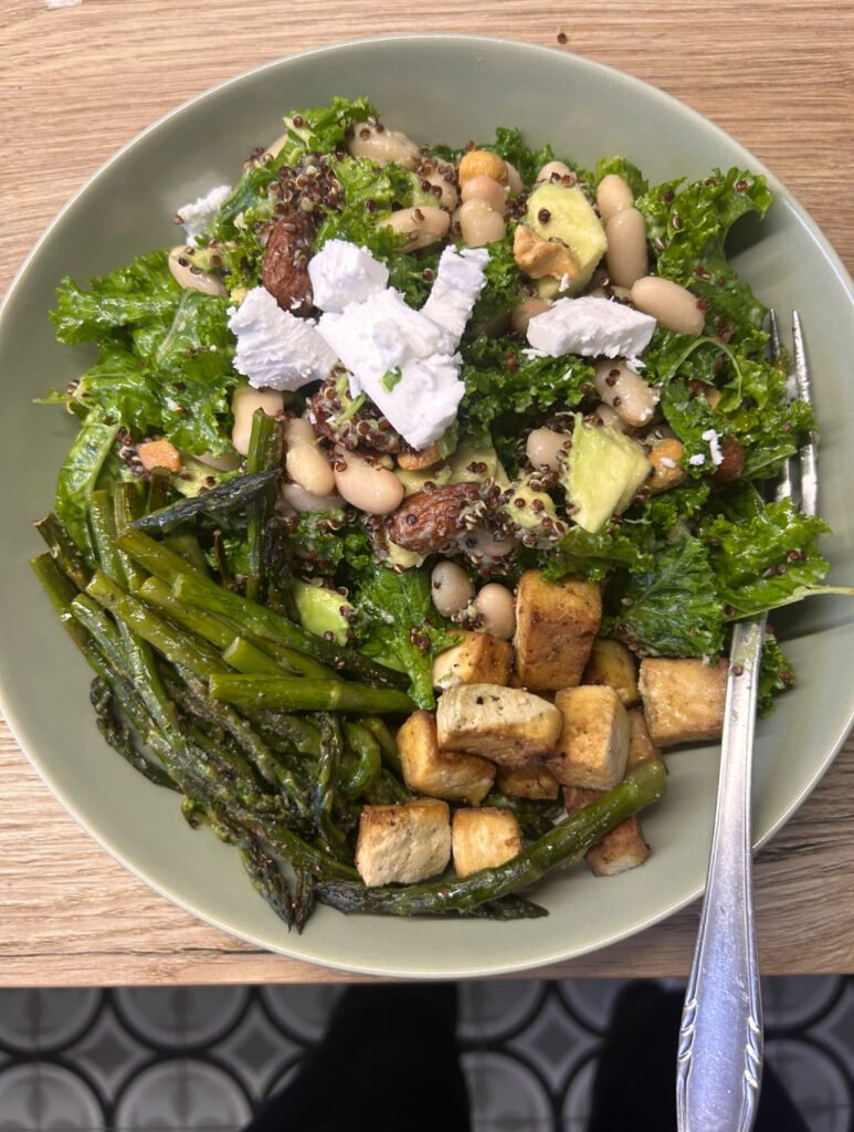 Hearty kale salad with white beans, red quinoa, avocado, tofu cubes, and roasted asparagus.