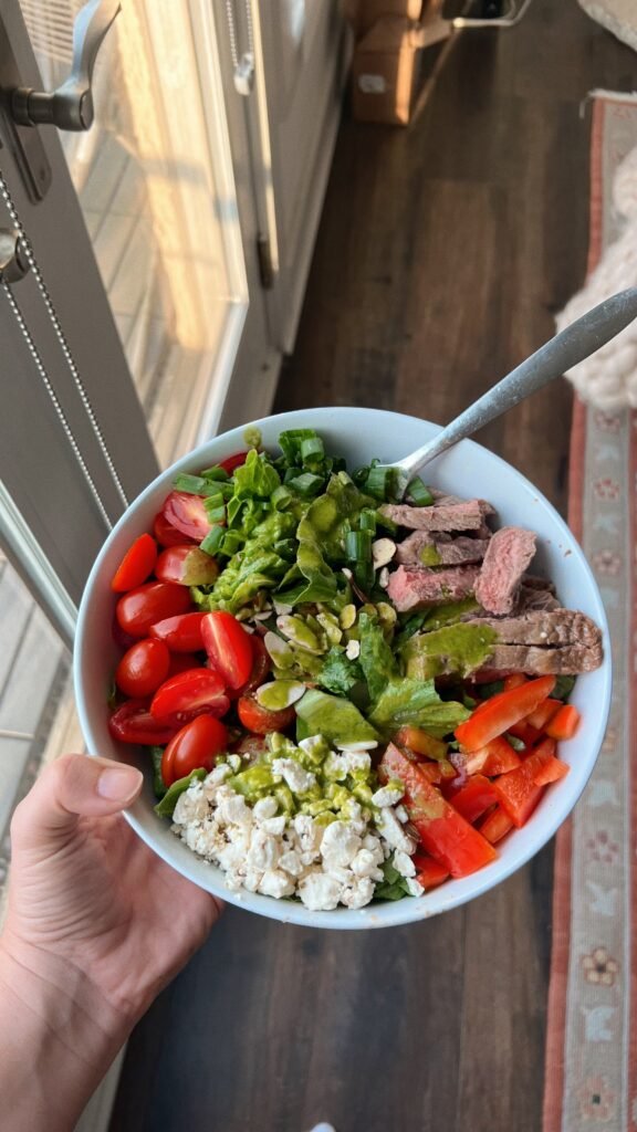 Loaded salad with cherry tomatoes, peppers, greens, feta, avocado, pepitas, and sliced steak.